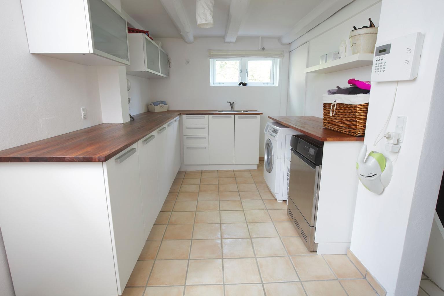 Praktisk och stilren tvättstuga efter renovering med vita skåp, träbänkskiva, tvättmaskin och gott om arbetsyta för tvätt och förvaring.