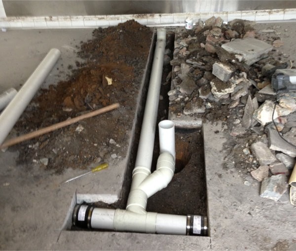 Arbete med att bila upp betonggolv för att byta golvbrunn och äldre gjutjärnsrör i tvättstuga i en bostadsrättsförening.